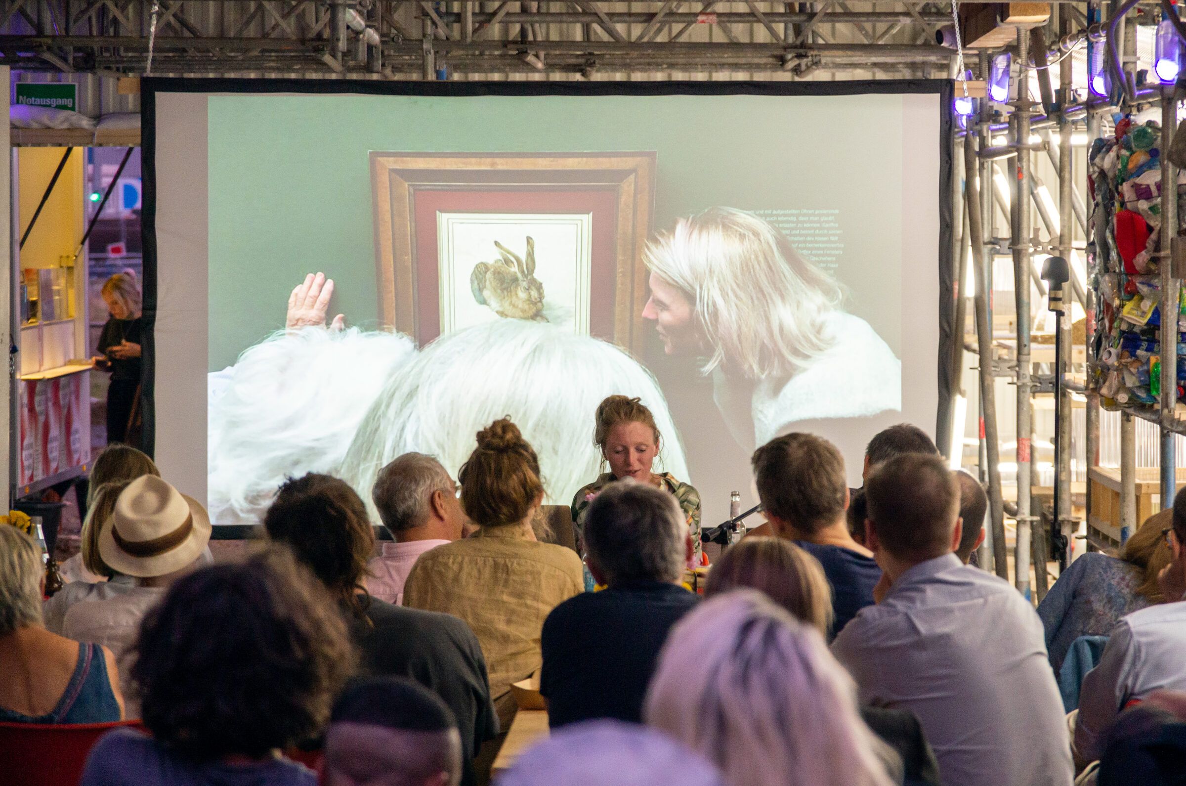 Publikum schaut auf eine große Leinwand mit einem projizierten Kunstwerk.