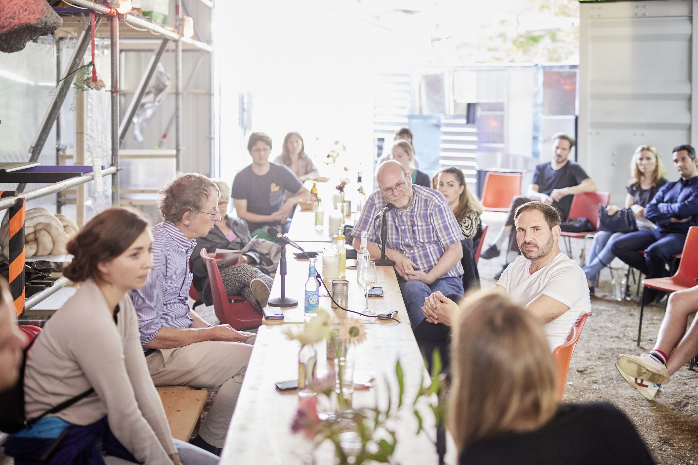 Blick entlang der langen Tafel, an der Teilnehmende im Gegenlicht sitzen und diskutieren.