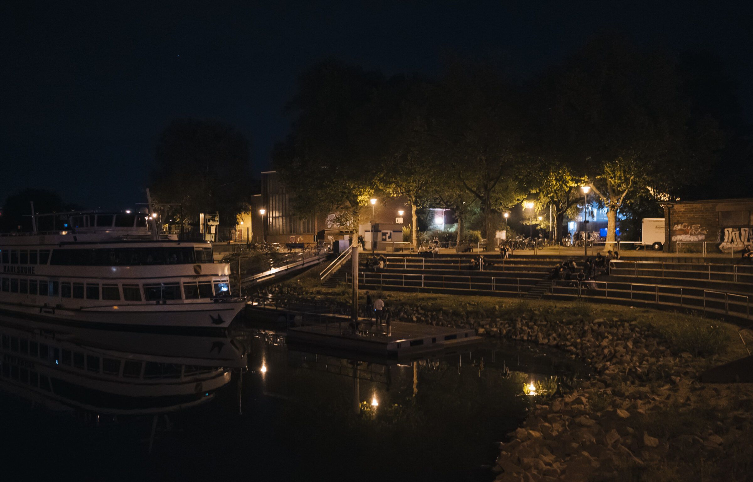 Das Hafenbecken bei Nacht, im Wasser spiegeln sich die Lichter eines Schiffs und des Ufers.