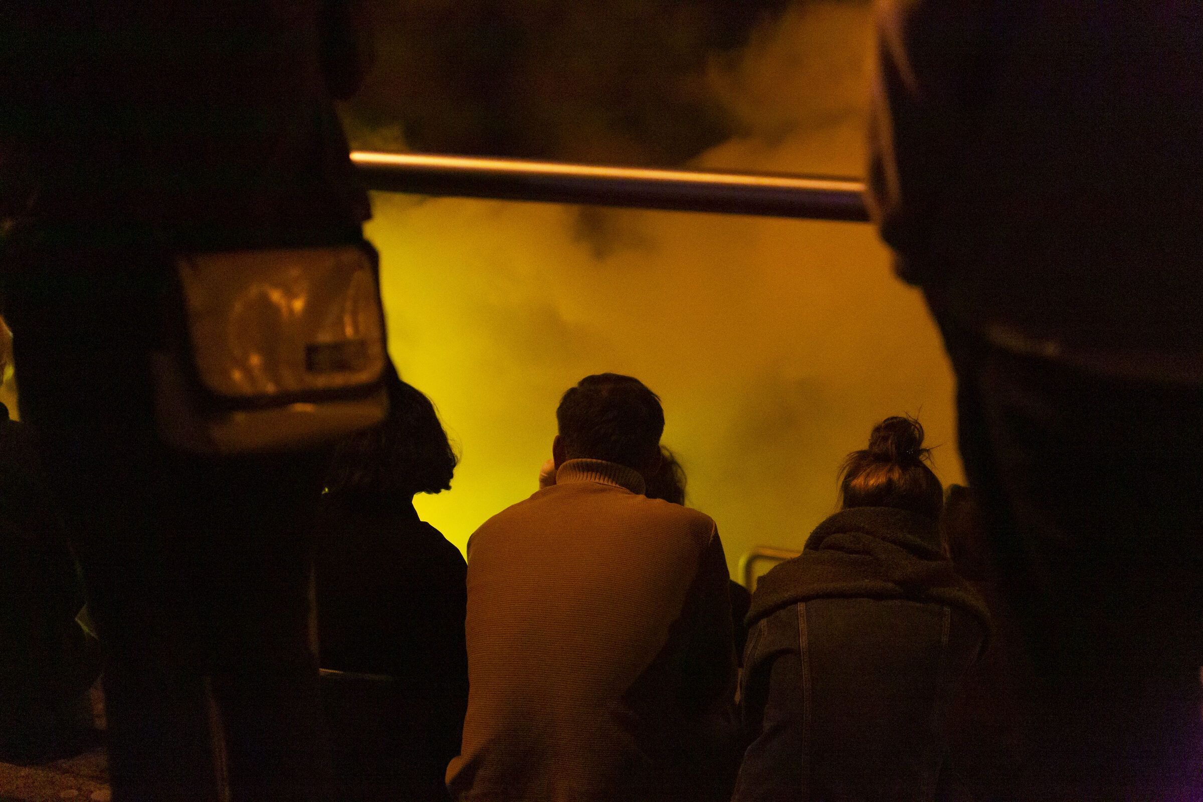 Zuschauende stehen als Silhouetten vor gelbem Rauch.