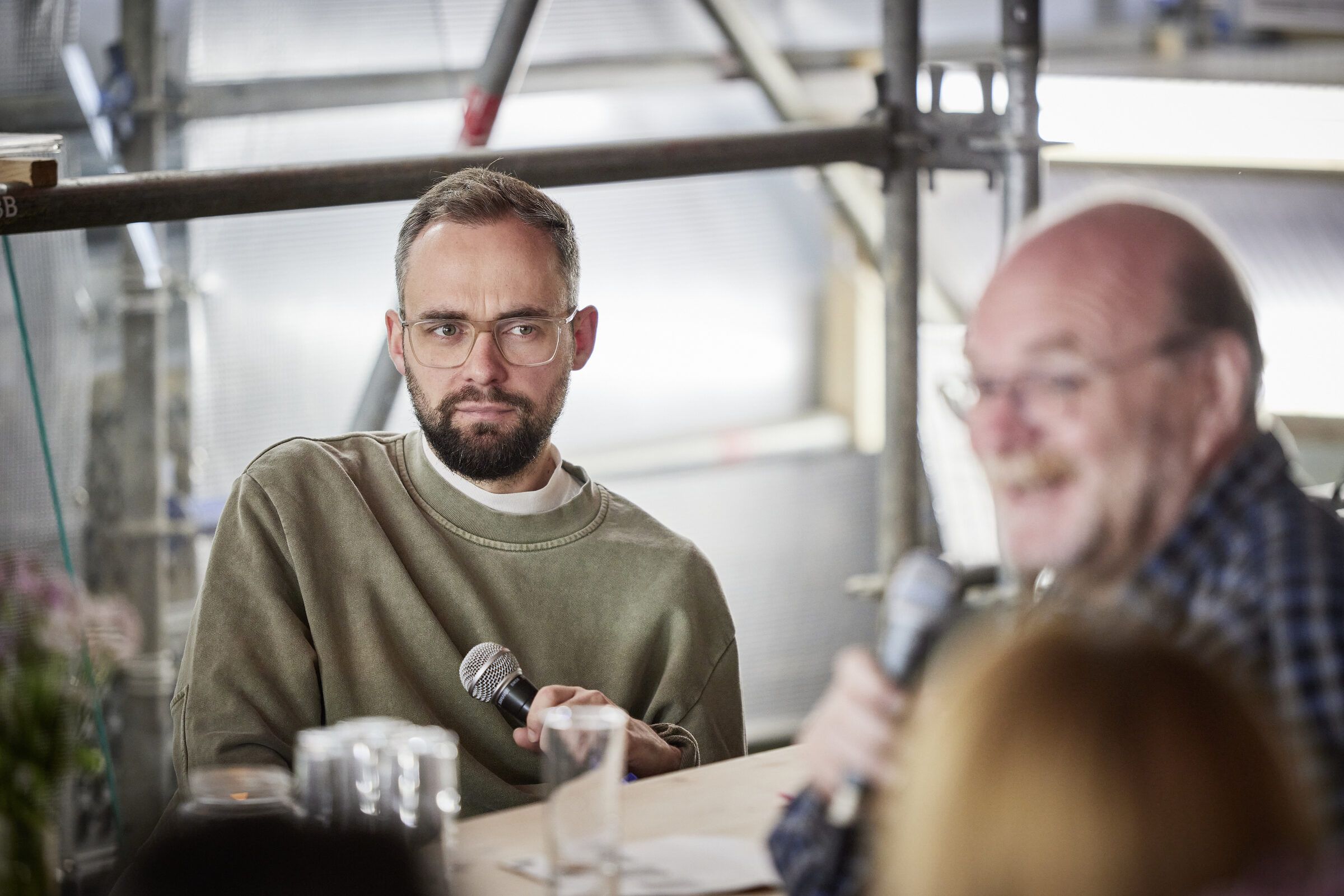 Zwei Gesprächsteilnehmer an der Tafel, einer spricht ins Mikrofon.