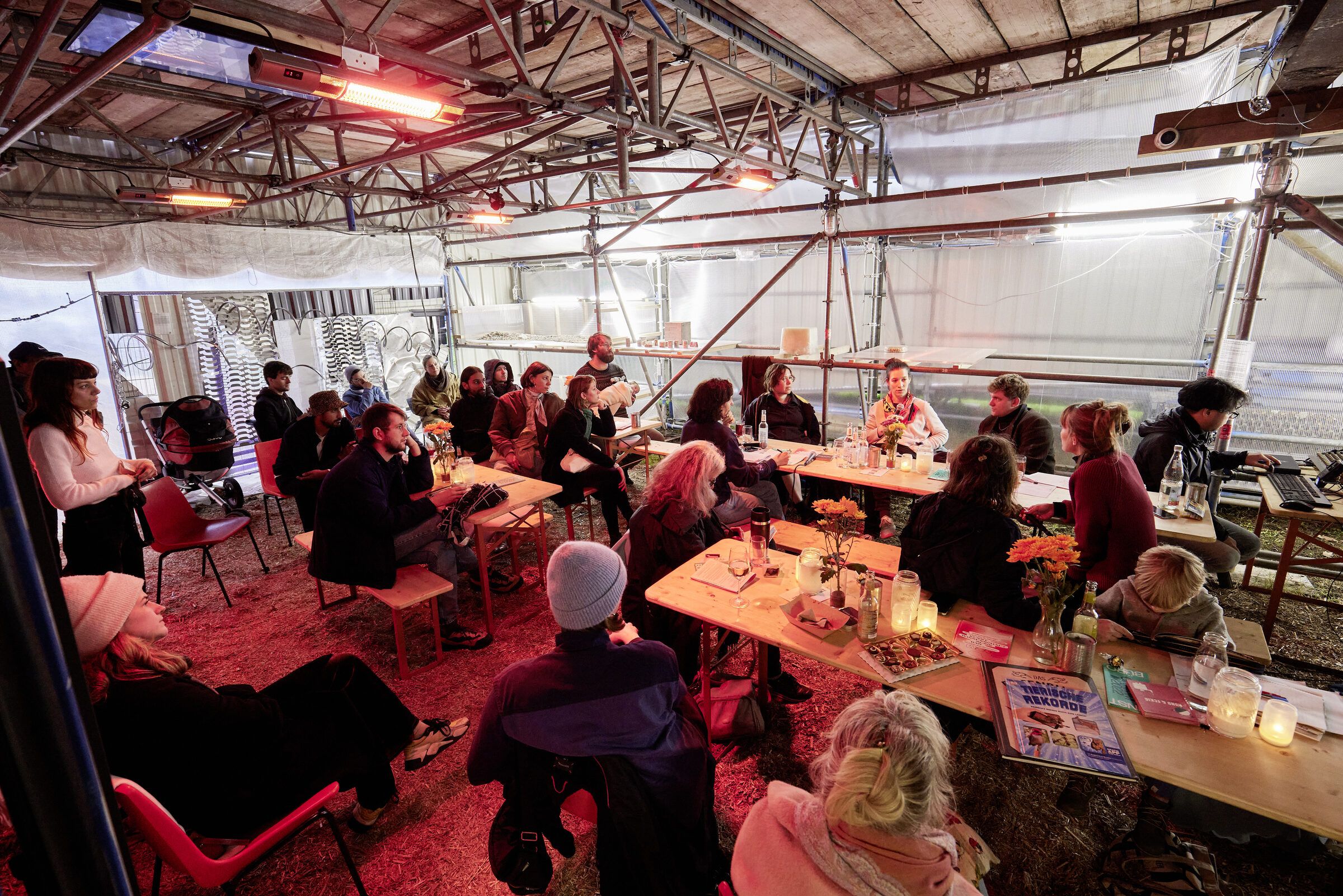 Zuhörende sitzen an Tischen verteilt in der Halle.