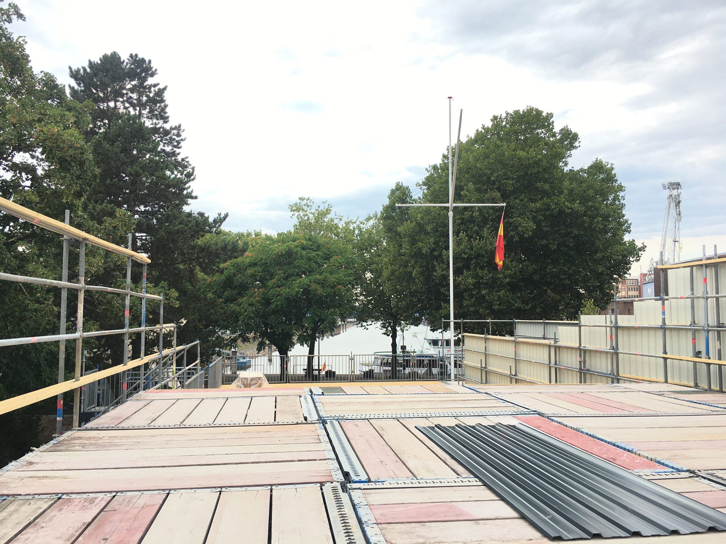 Das Dach im Aufbau mit Platten, Blechen und Geländer, im Hintergrund Bäume und ein Fahnenmast.