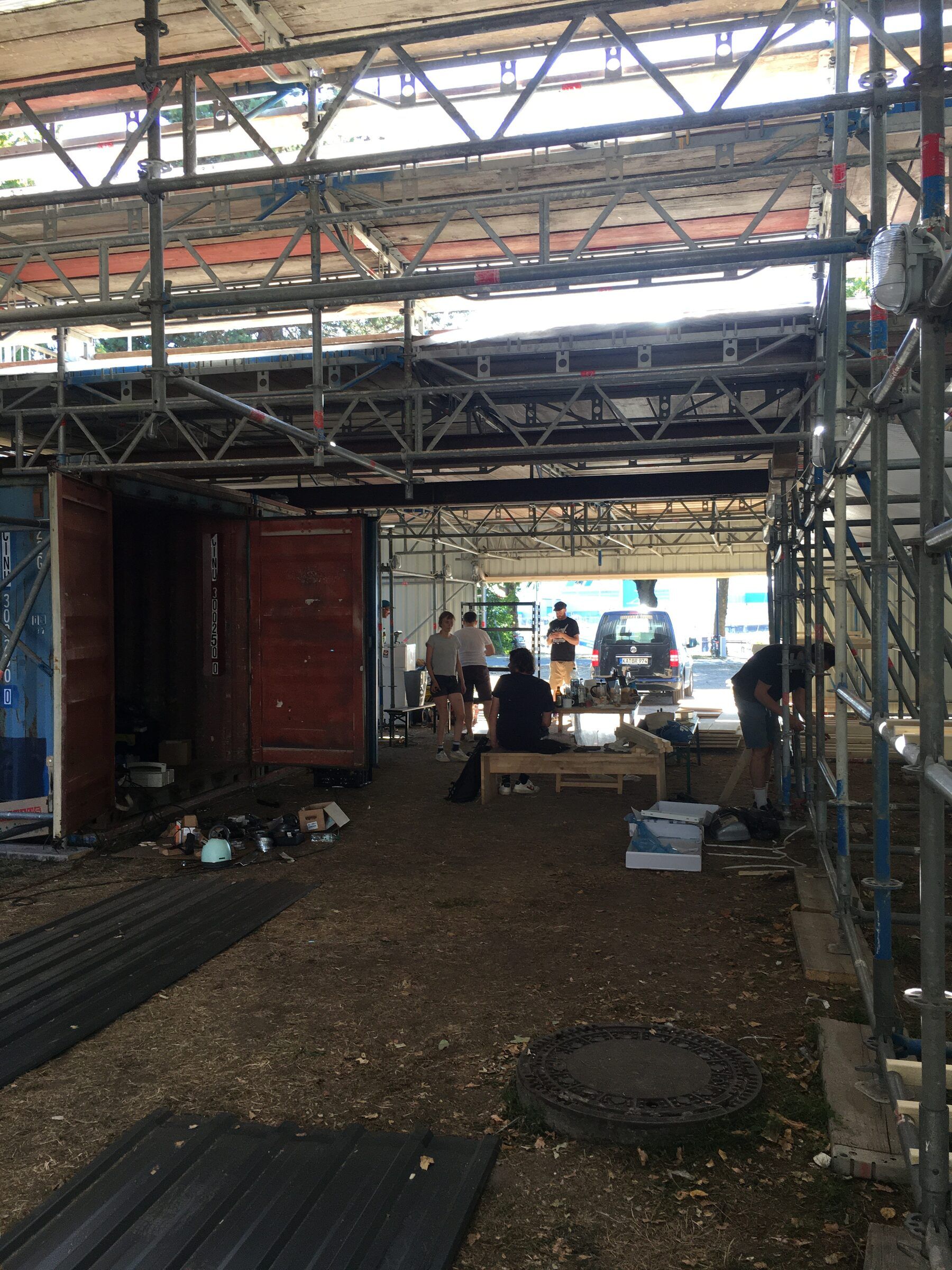 Blick in das Erdgeschoss im Rohbau mit Gerüstdach, Containern und Material auf dem Boden.