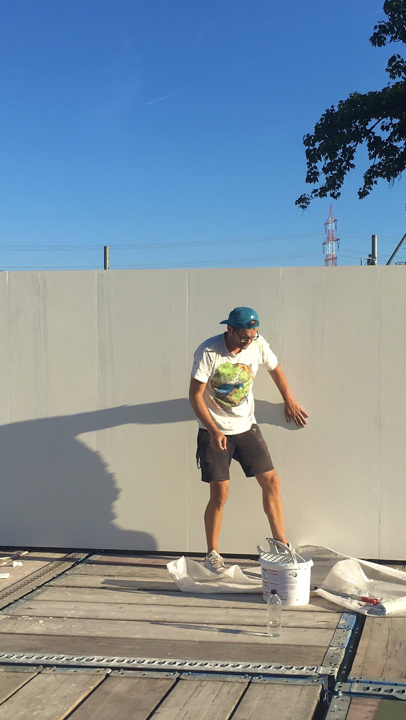 Eine Person streicht auf dem Dach eine weiße Wand, daneben steht ein Farbeimer.