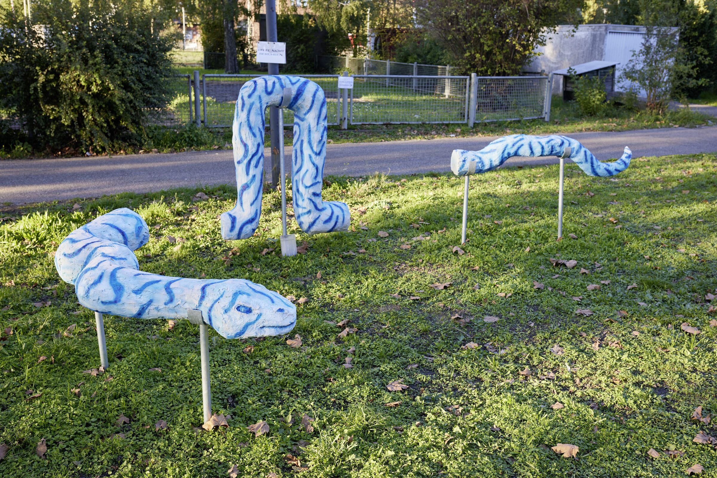 Mehrere blau-weiße Skulpturen in Schlaufenform verteilen sich auf der Wiese am Gelände.