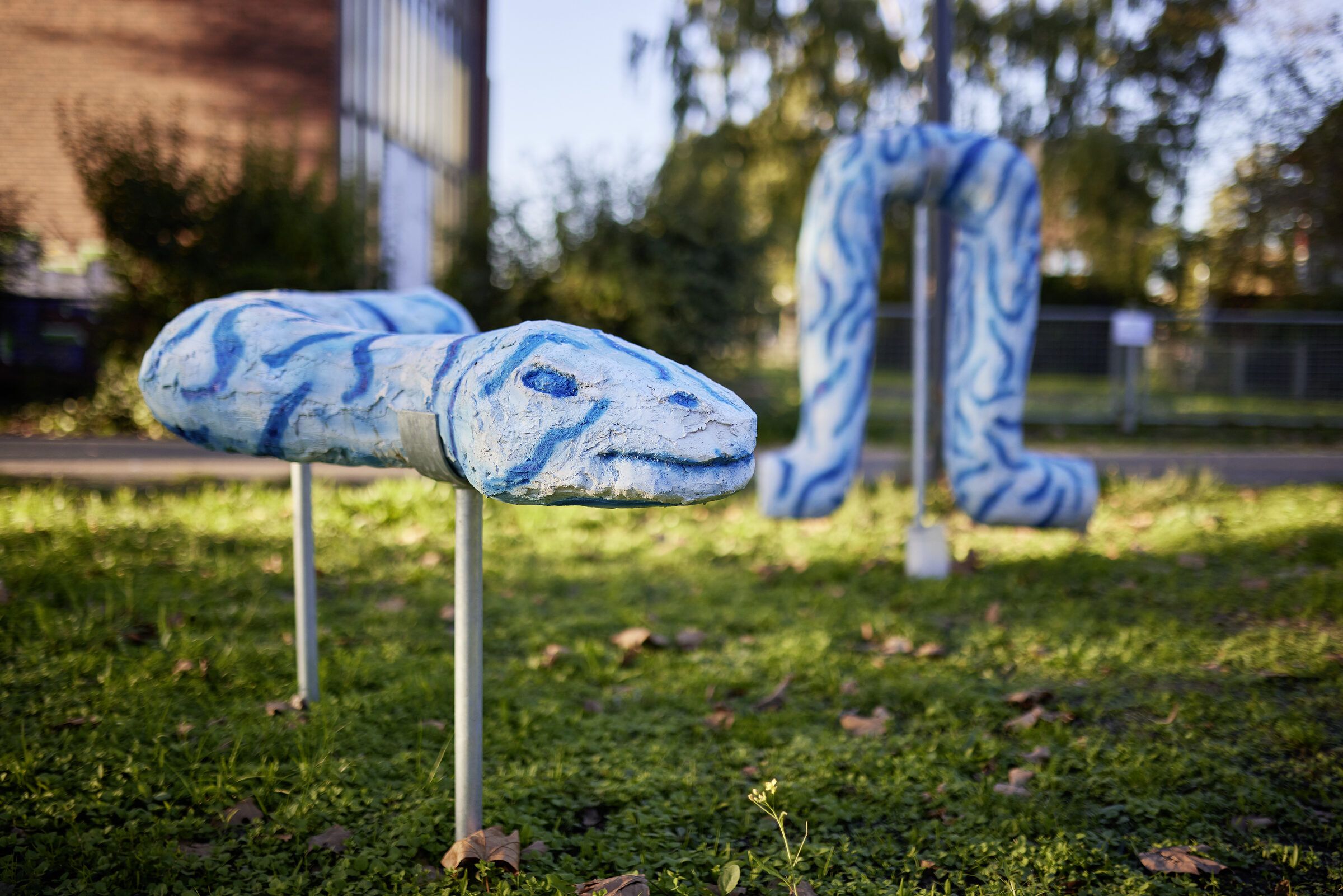 Blau-weiß gemusterte, wurmartige Skulpturen stehen auf Stelzen auf einer Wiese.