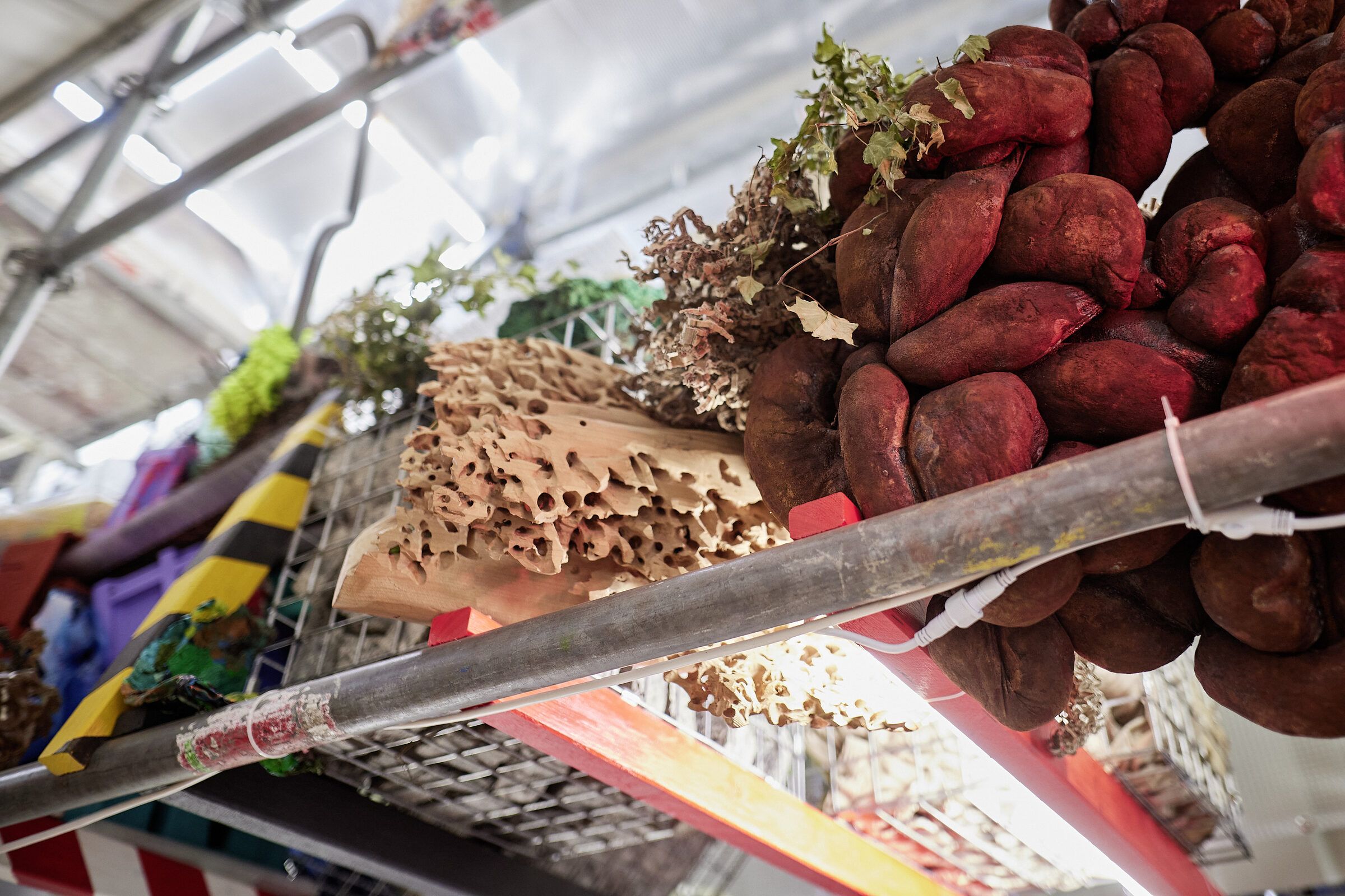 Nahaufnahme eines Regalfachs mit roten Knollen, Holzfasern und bunten Resten zwischen Gerüstrohren.