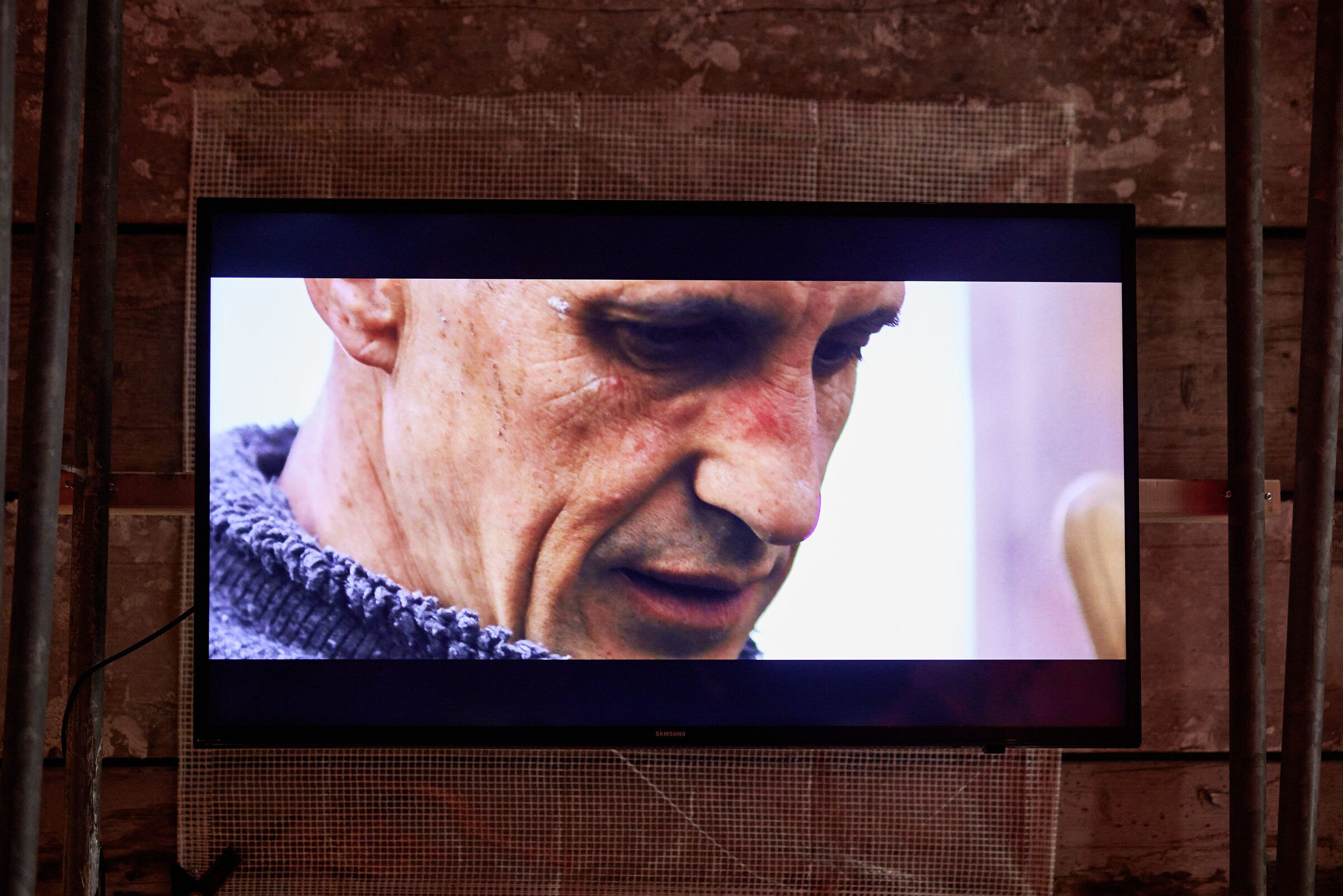 Ein Monitor zeigt das Gesicht eines Mannes mit gesenktem Blick.