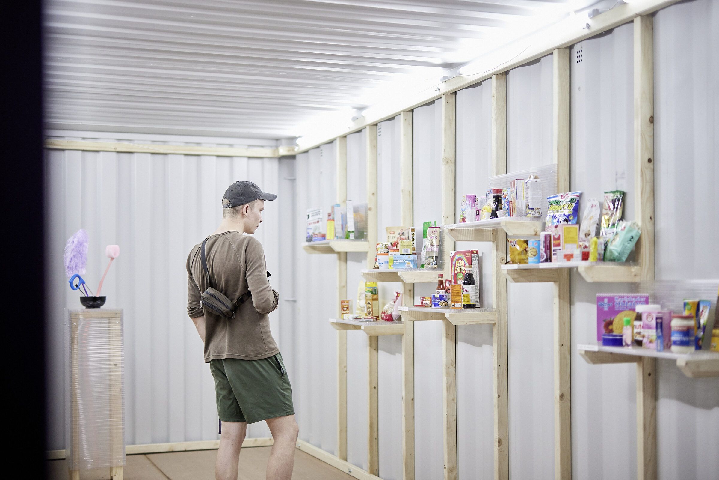 Ein Besucher betrachtet im weißen Container Wandregale mit Konsumprodukten.