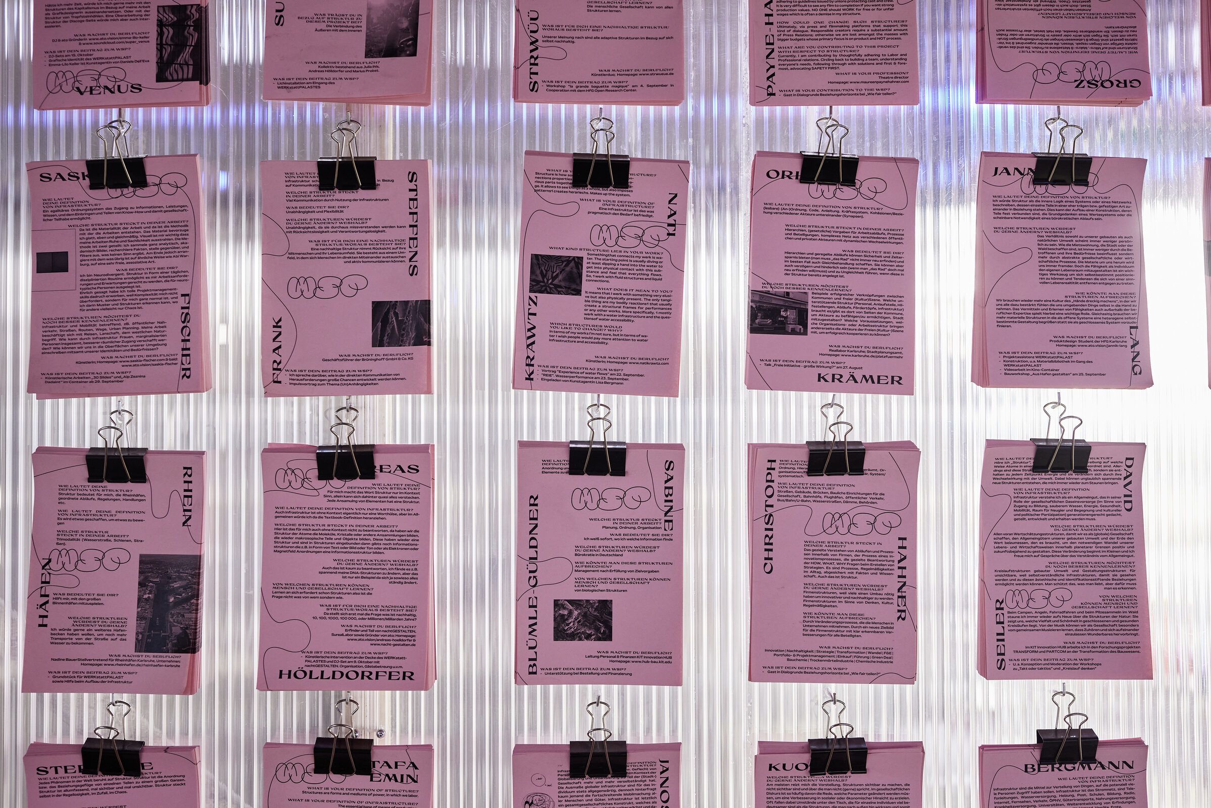 Rosa Fragebögen hängen in Reihen mit schwarzen Klammern an der Wand.